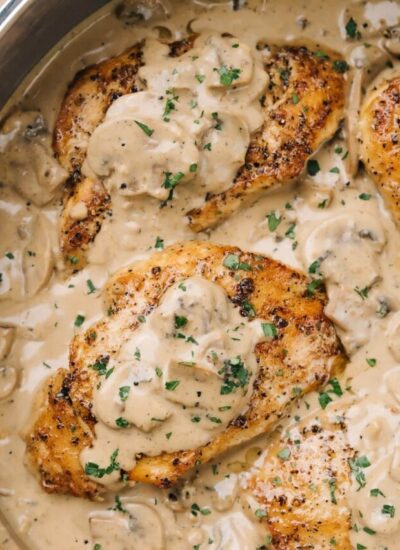 Chicken with creamy mushroom sauce topped with fresh chopped parsley in a stainless steel skillet.