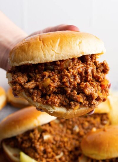 A hand holding a hamburger bun generously stuffed with homemade Sloppy Joes.