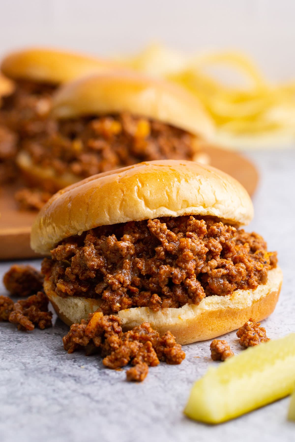 Several homemade Sloppy Joes sandwiches with pickle spears and potato chips.