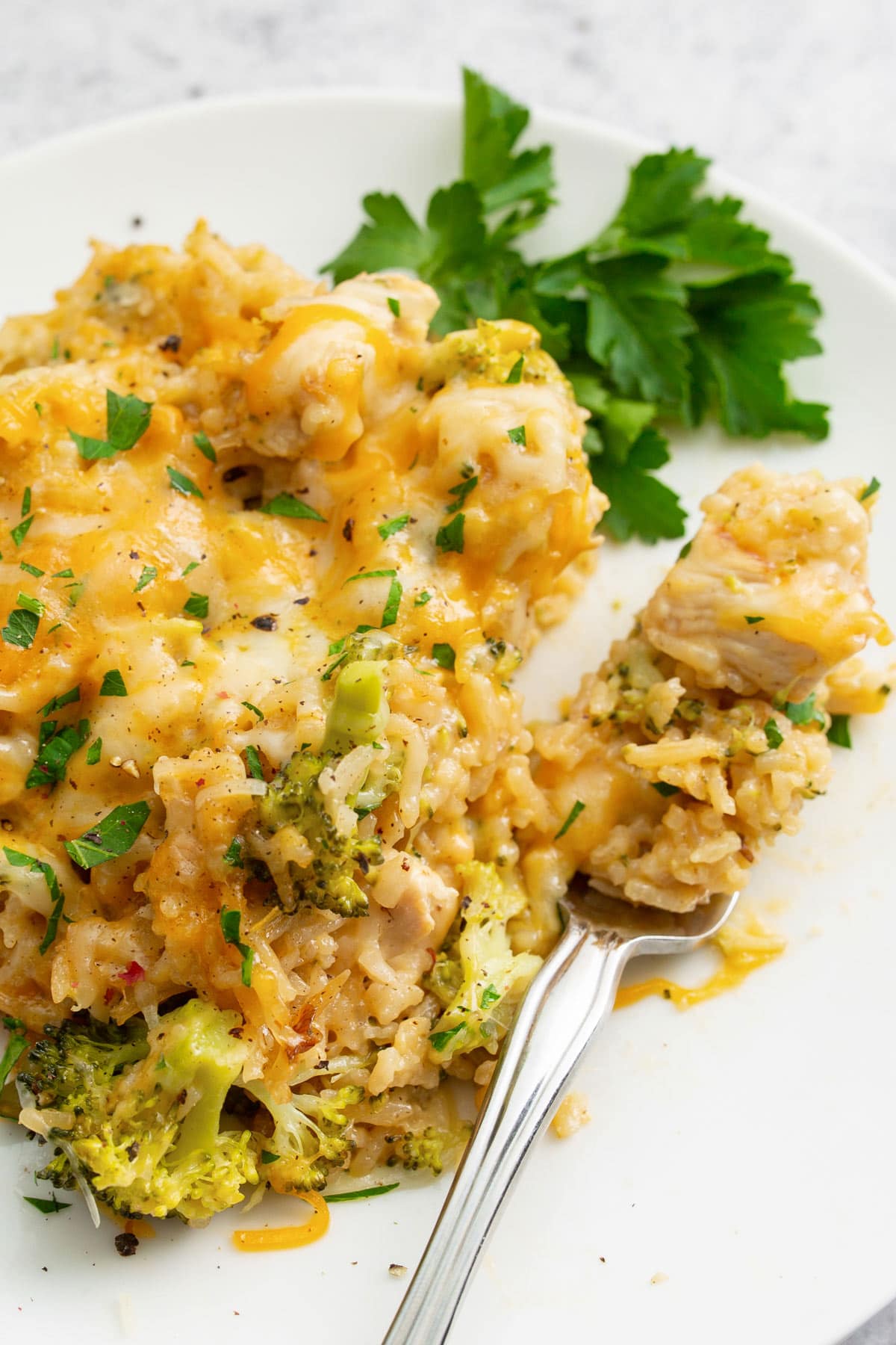 A generous serving of chicken broccoli rice casserole on a white plate topped with fresh parsley.