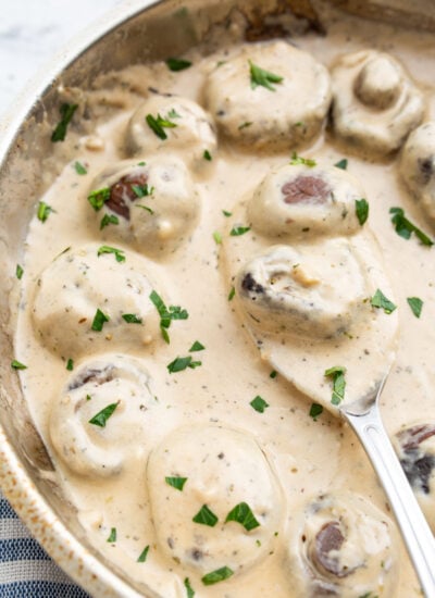 Creamy garlic mushrooms topped with fresh chopped parsley in a stainless steel skillet.