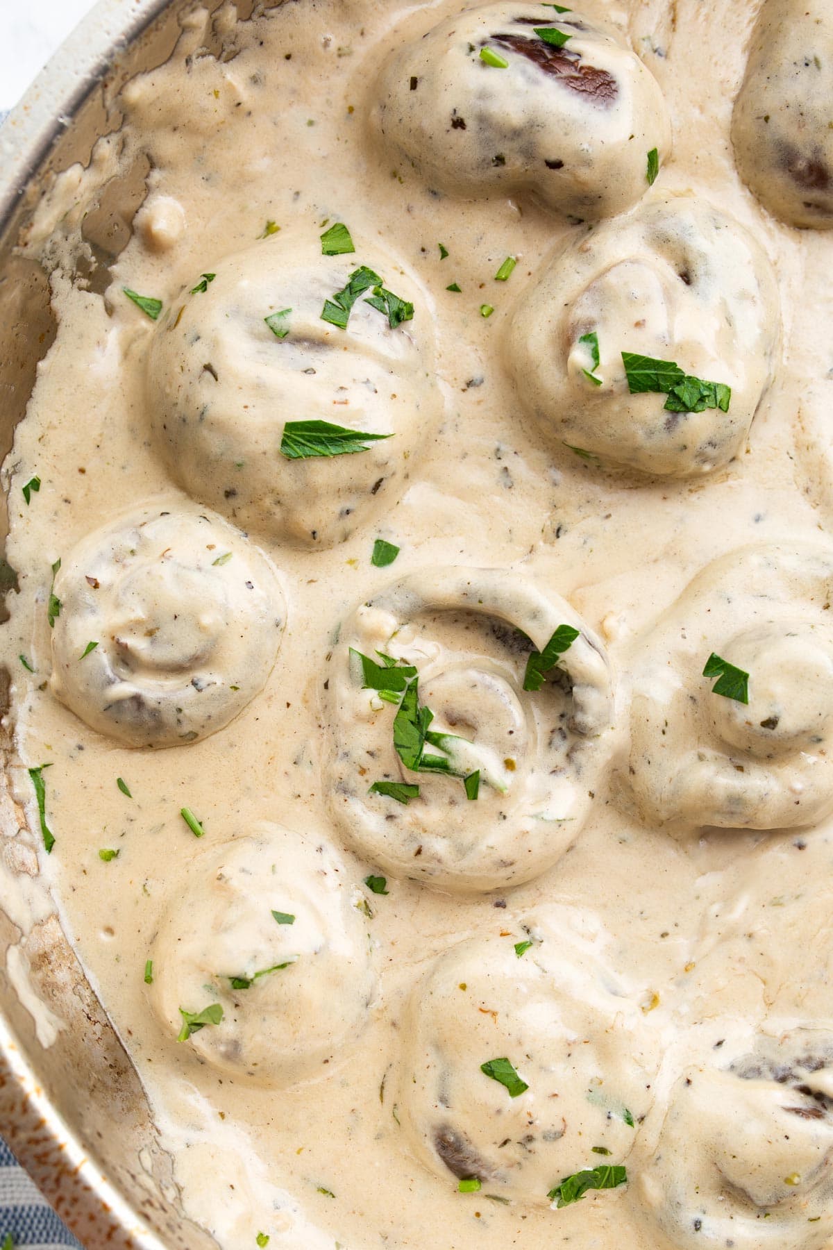 Creamy garlic mushrooms topped with fresh chopped parsley in a stainless steel skillet.
