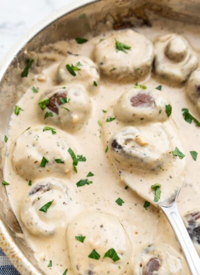 Creamy garlic mushrooms topped with fresh chopped parsley in a stainless steel skillet.