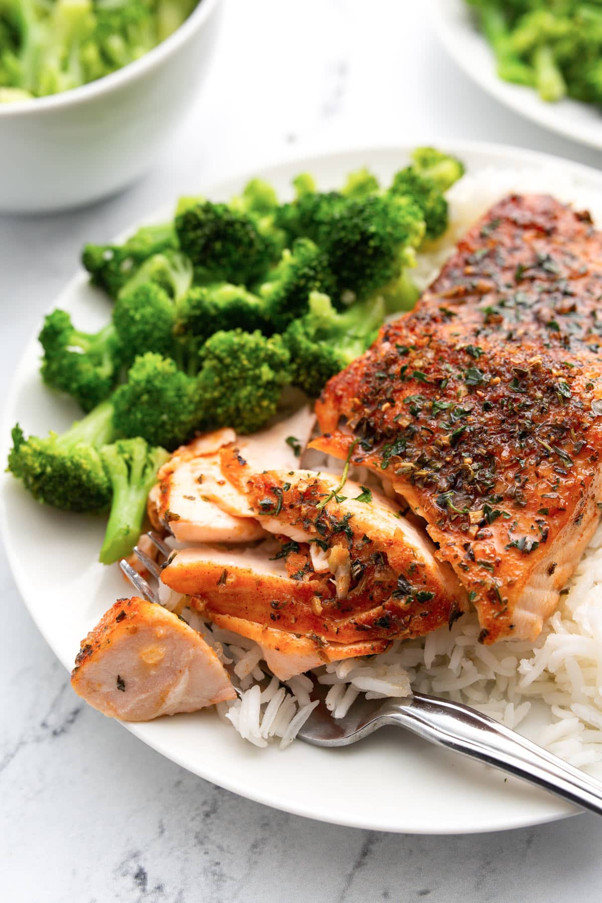 Easy air fryer salmon on a white dinner plate served with a side of white rice and broccoli.