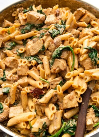Creamy Tuscan chicken pasta in a stainless steel skillet.