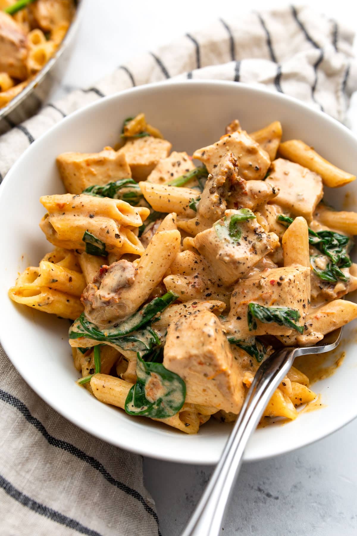 Creamy Tuscan chicken pasta with a fork in a single-serving white bowl.