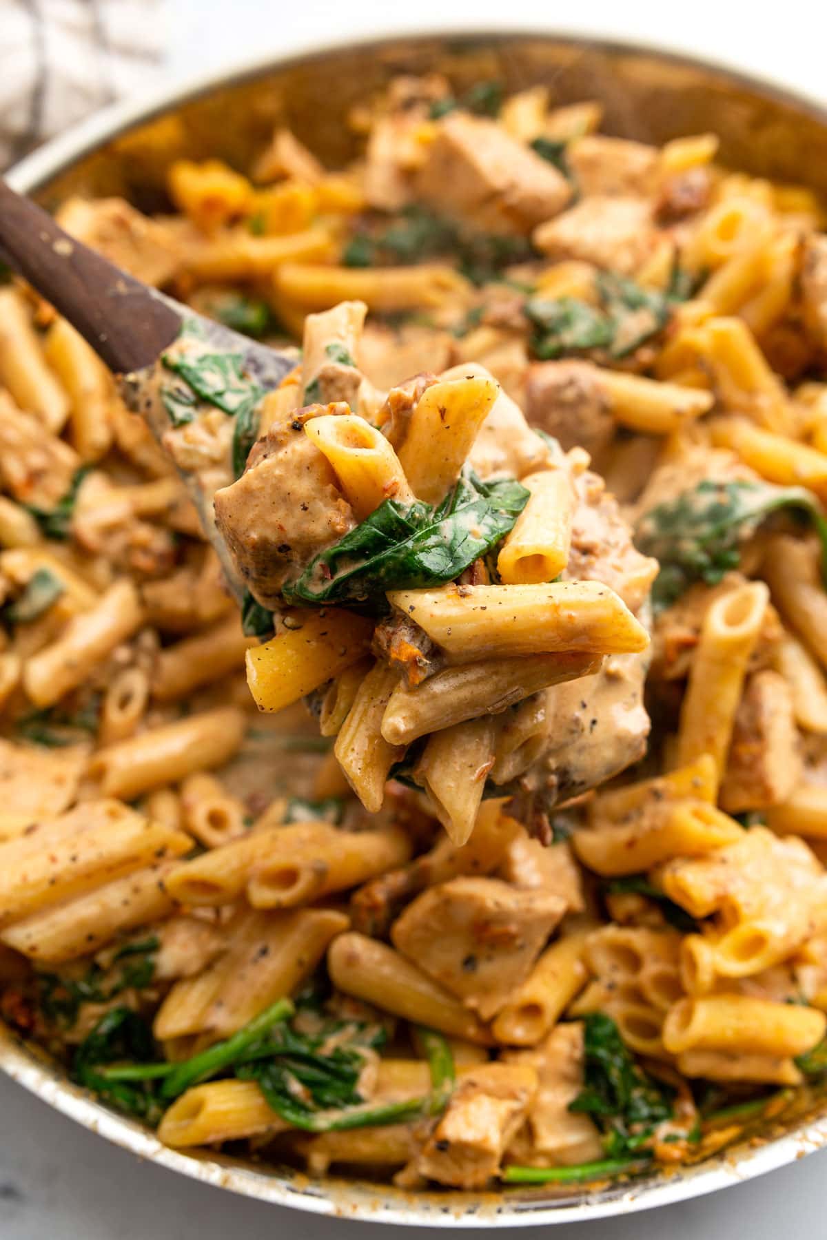 A generous portion of creamy Tuscan chicken pasta on a wooden serving spoon.