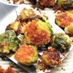 Several roasted crispy garlic Parmesan brussels sprouts scattered across a baking sheet.