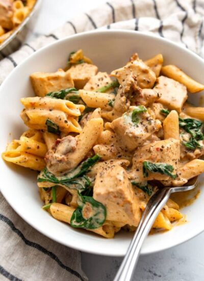 Creamy Tuscan chicken pasta with a fork in a single-serving white bowl.