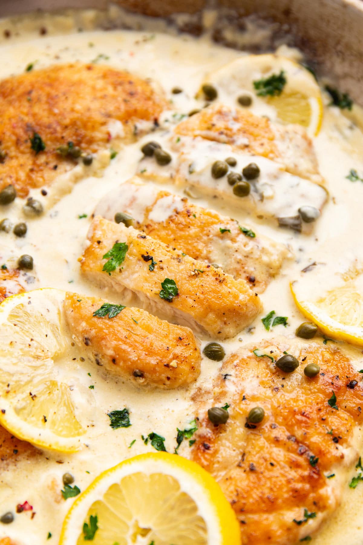 Creamy lemon chicken piccata in a stainless steel skillet topped with lemon slices and chopped fresh parsley.