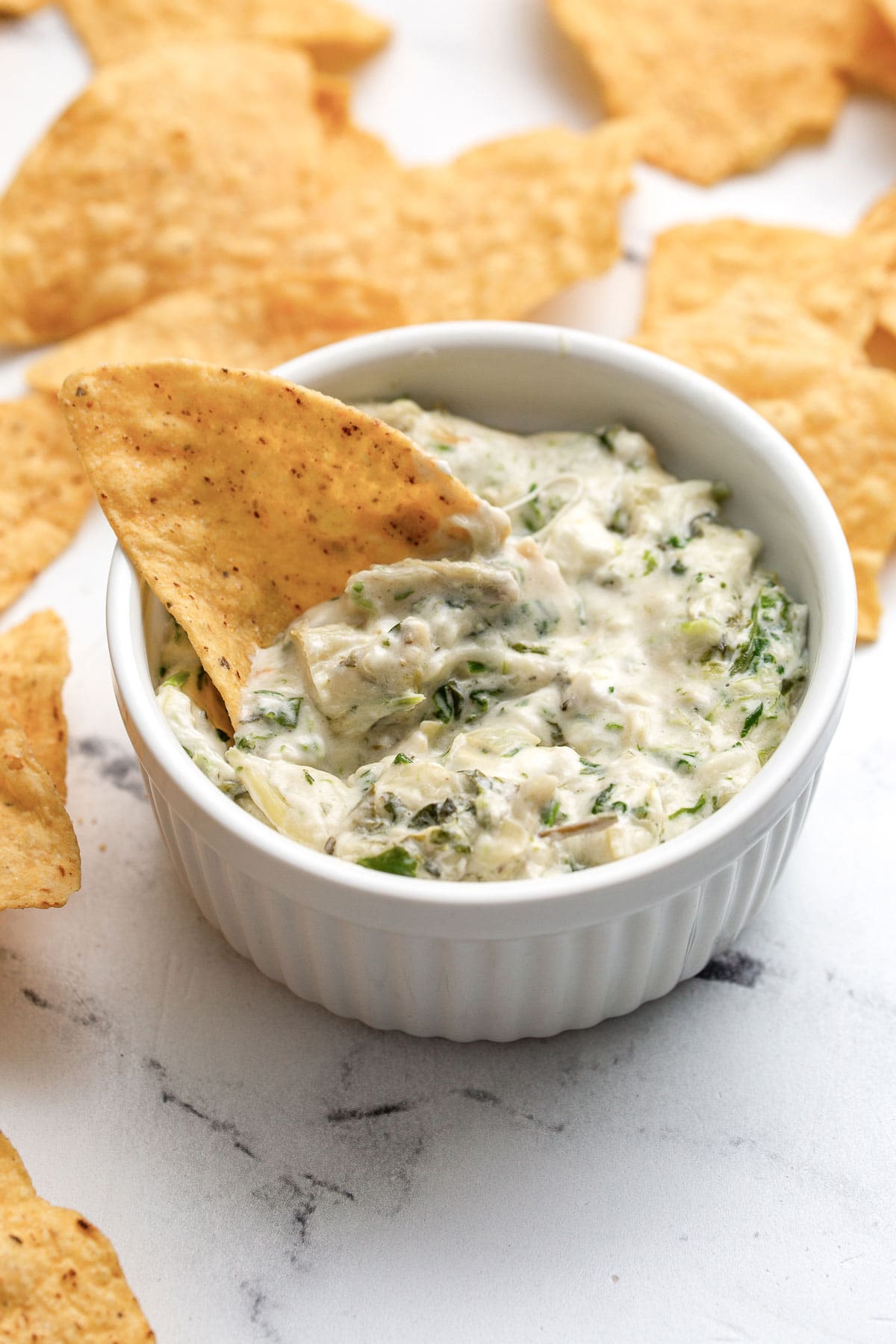 Spinach and artichoke dip in a white ramekin surrounded by tortilla chips.