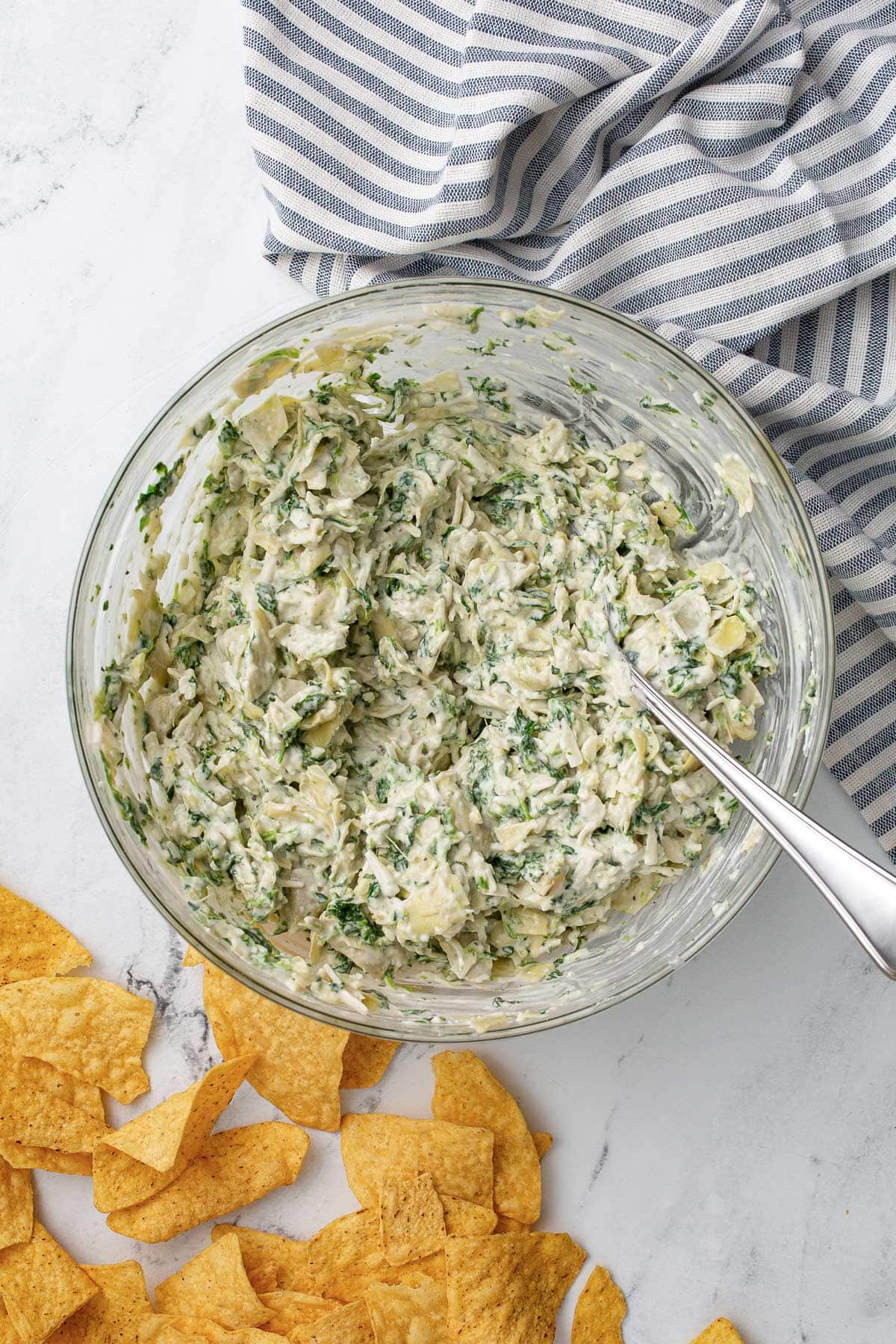Combining the raw ingredients for spinach and artichoke dip in a glass mixing bowl.