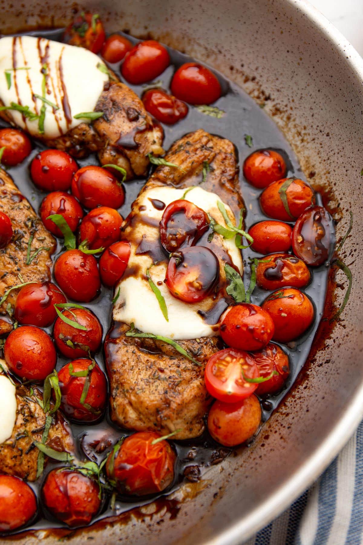Caprese chicken and cherry tomatoes in a skillet smothered in a balsamic reduction topped with fresh basil.