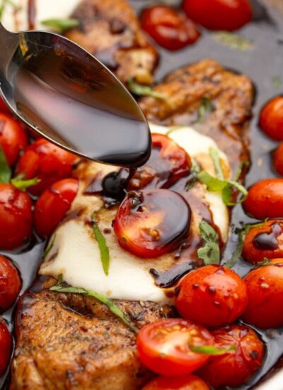 Caprese chicken and cherry tomatoes in a skillet smothered in a balsamic reduction topped with fresh basil.
