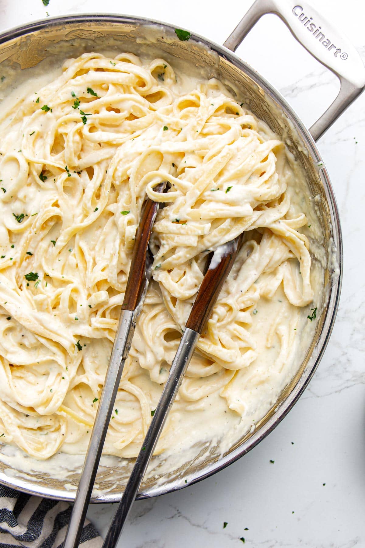 Fettucine pasta smothered in homemade Alfredo sauce in a stainless steel skillet.