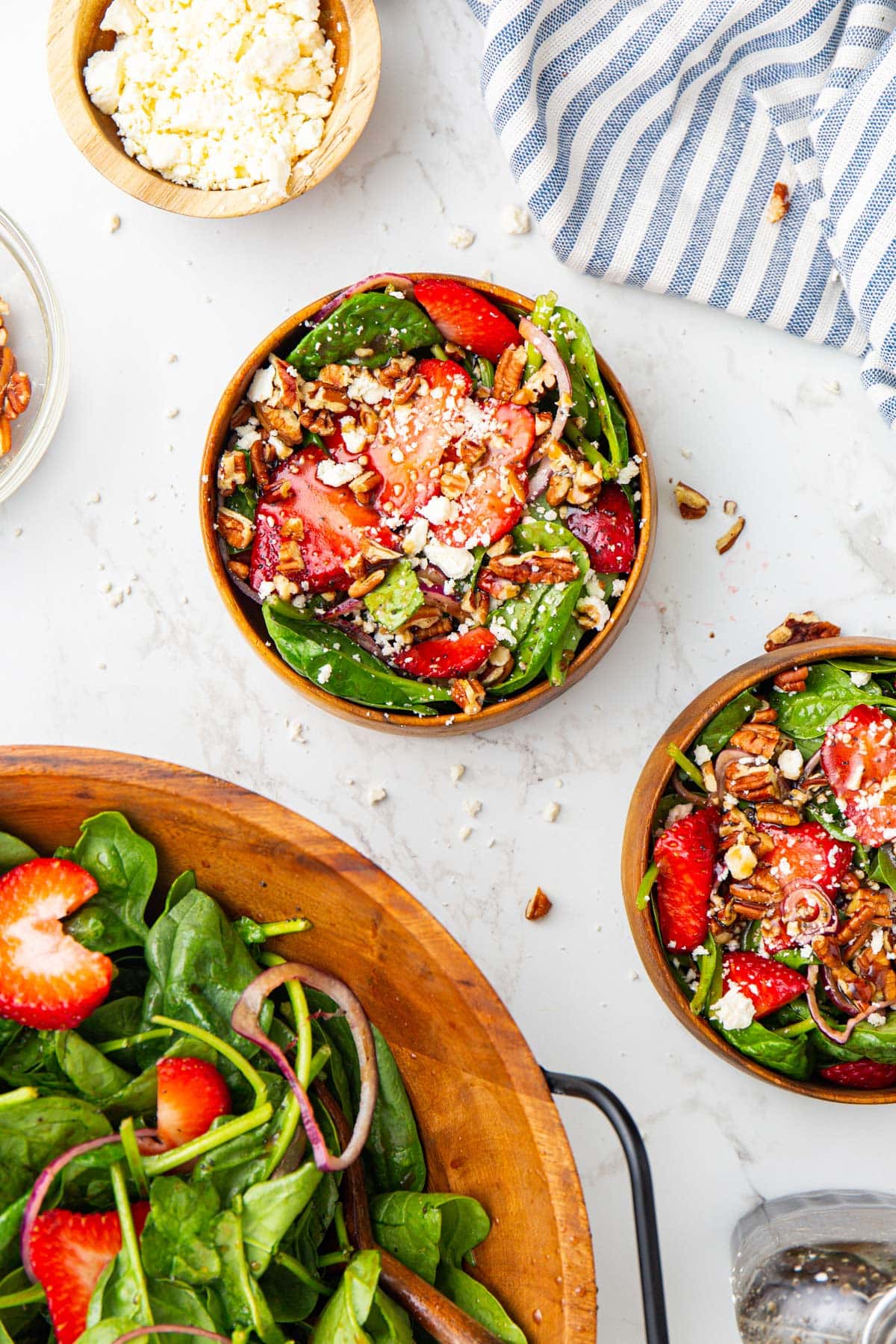 Spinach strawberry salad in two wooden bowls topped with feta cheese and pecans.