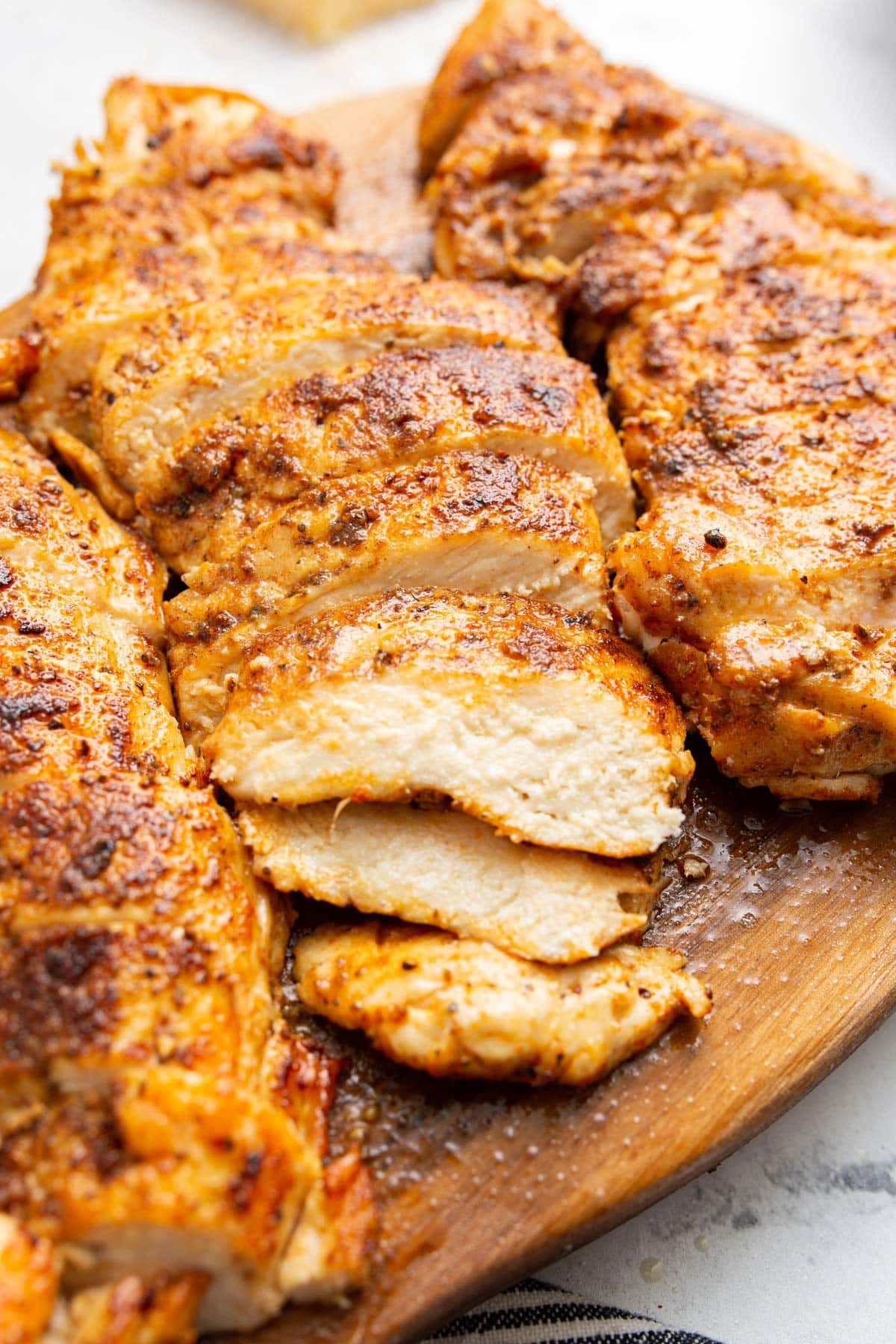 Thick slices of seared Cajun seasoned chicken on a cutting board.