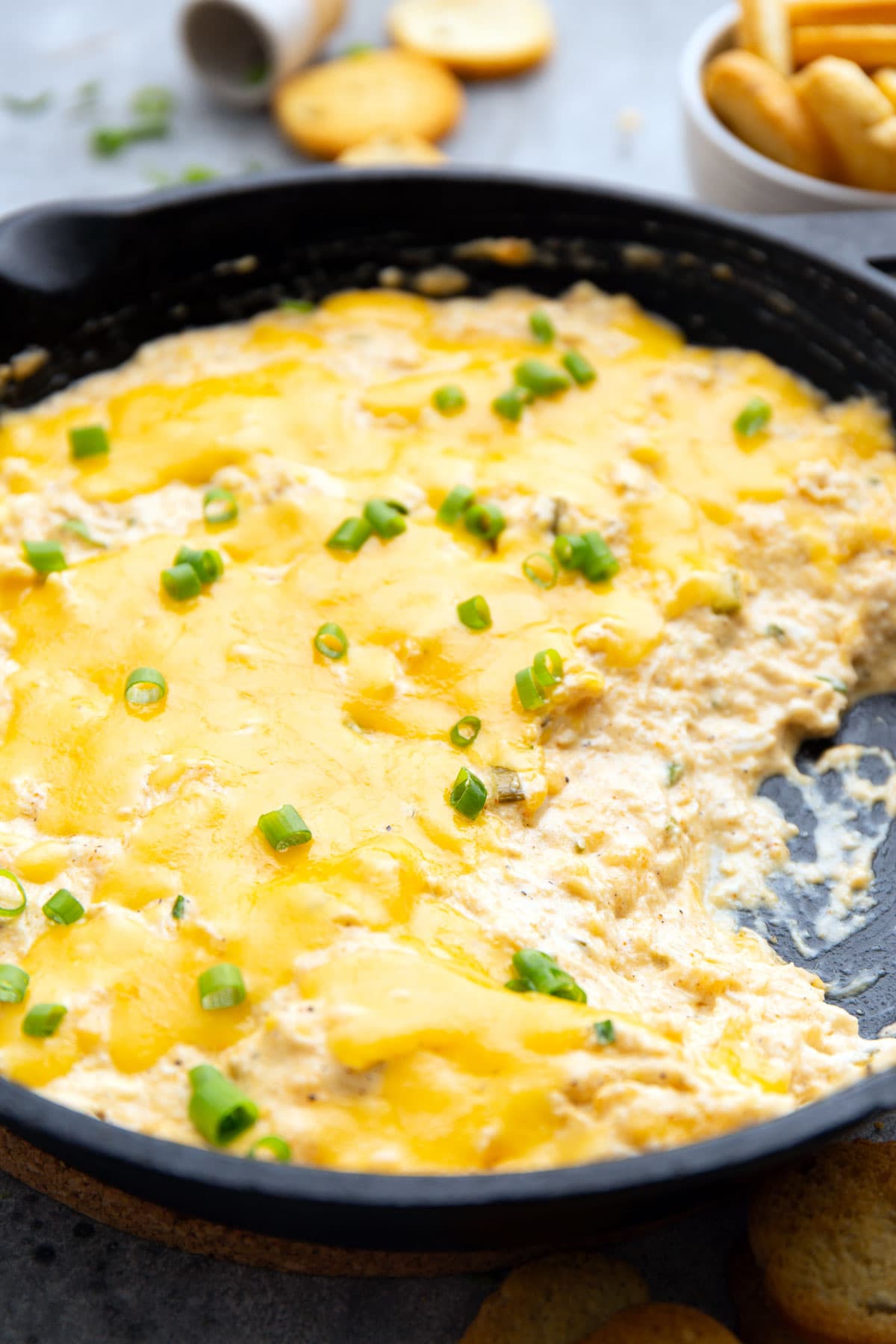Hot crab dip topped with melted cheddar cheese and green onions in a cast iron pan.