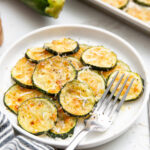 Roasted Parmesan zucchini stacked on a white plate and topped with freshly grated Parmesan cheese.
