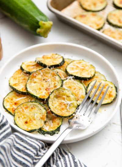 Roasted Parmesan zucchini stacked on a white plate and topped with freshly grated Parmesan cheese.