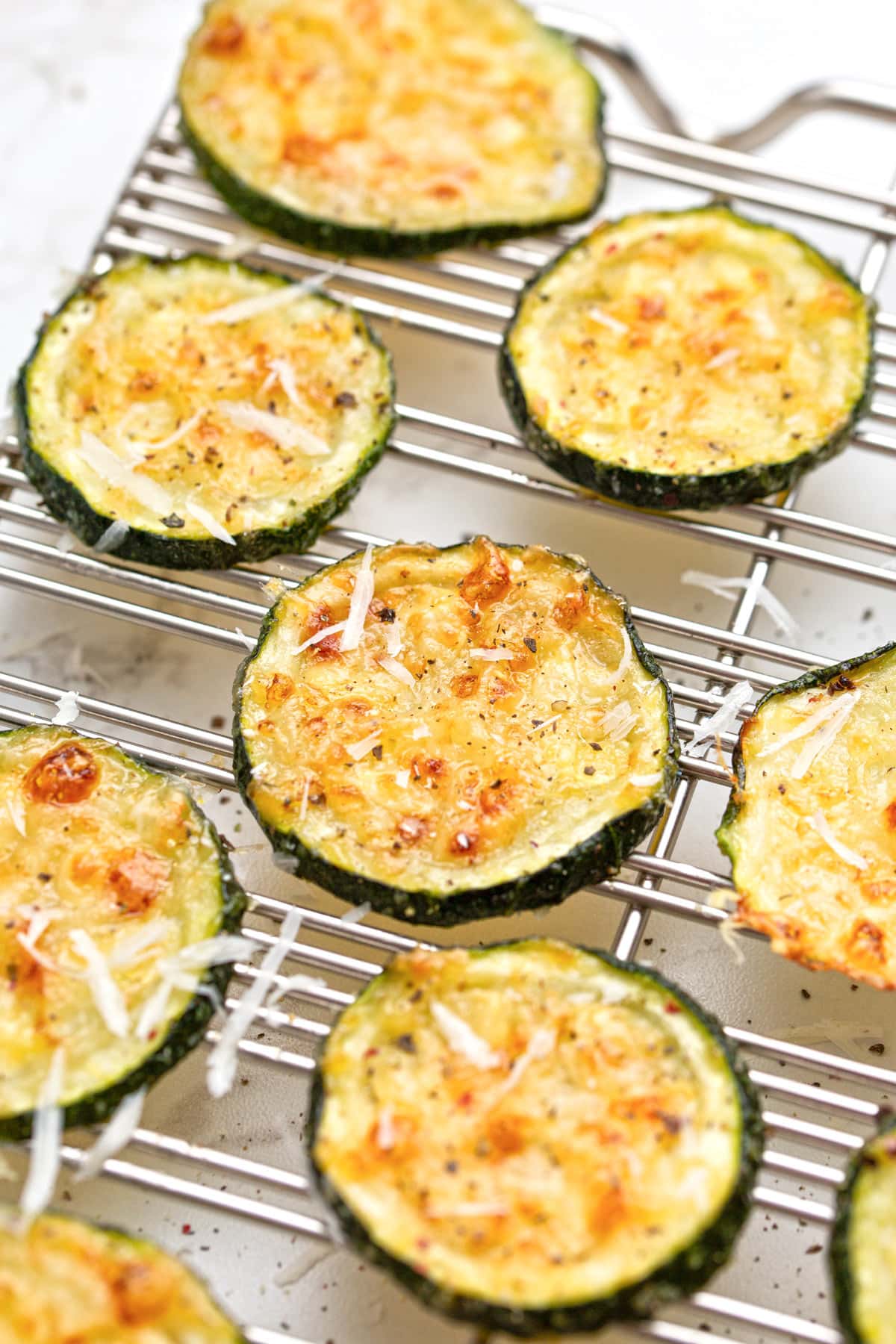 Roasted Parmesan zucchini arranged on a baking rack and topped with freshly grated Parmesan cheese.
