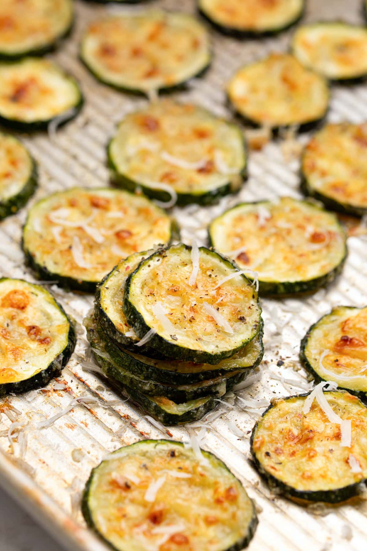 Roasted Parmesan zucchini on a ribbed baking sheet topped with freshly grated Parmesan cheese.