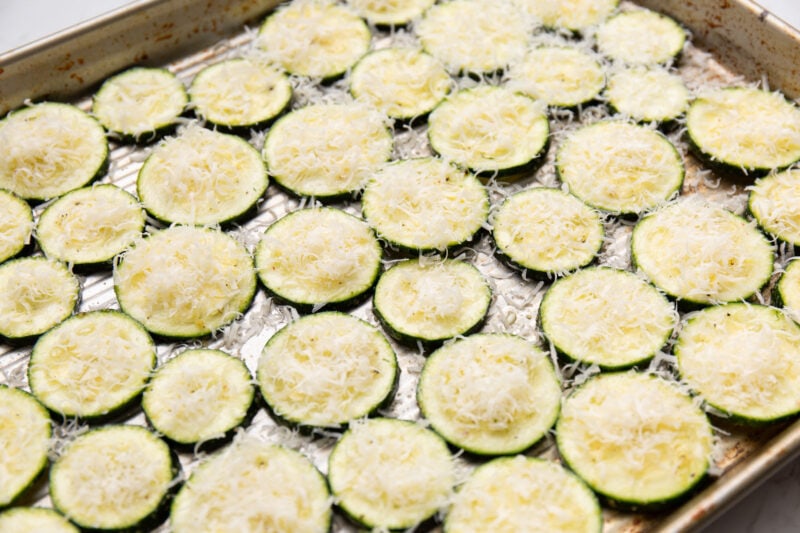 Zucchini rounds on a ribbed baking sheet topped with grated Parmesan cheese.