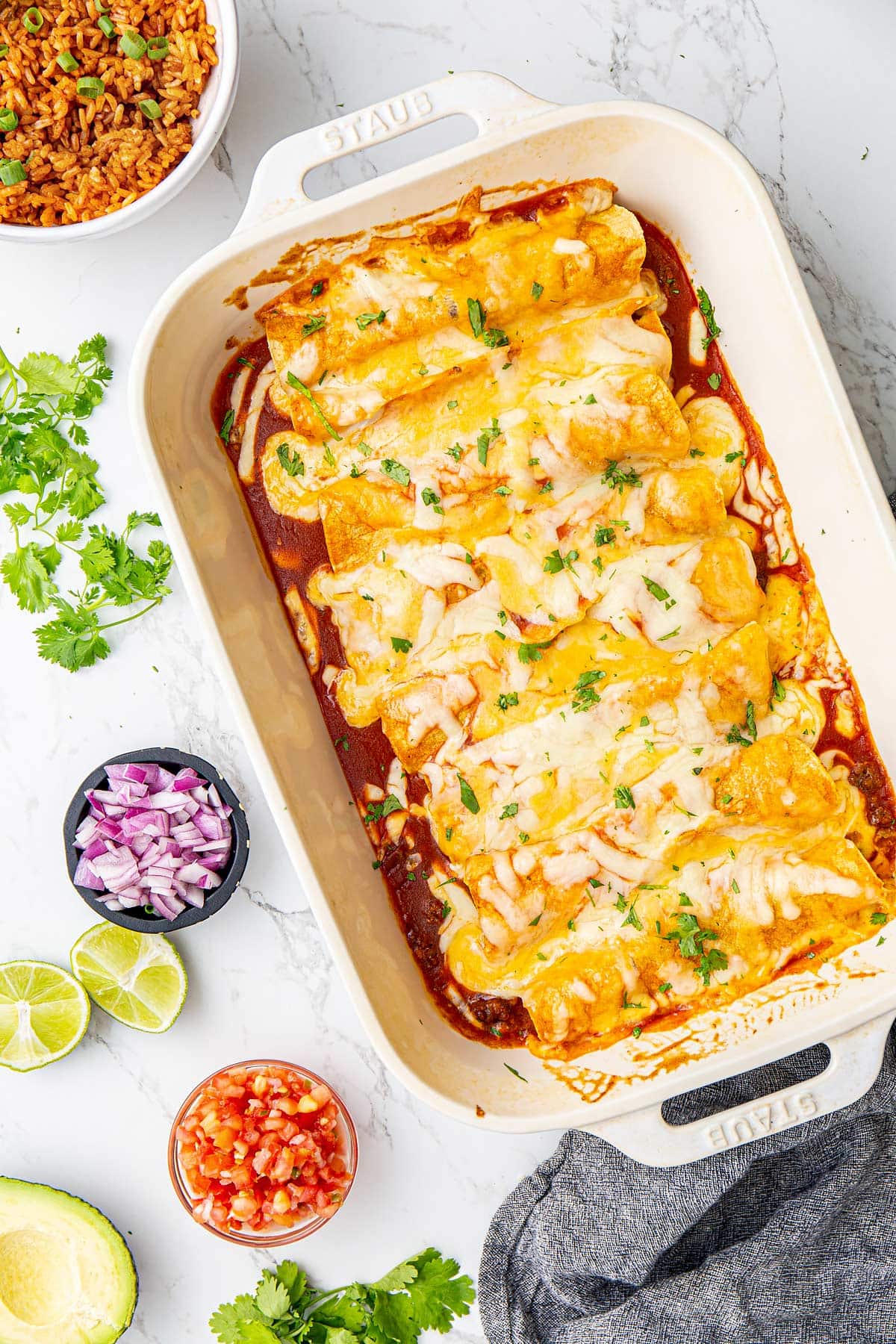 Beef enchiladas topped with enchilada sauce and cheese arranged in a white casserole dish.