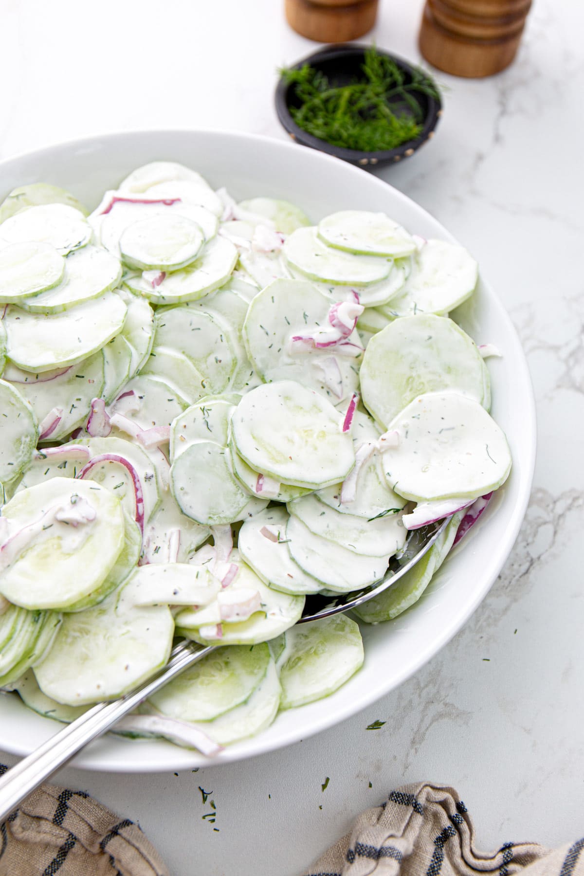 Creamy cucumber salad in a white serving bowl topped with fresh dill.