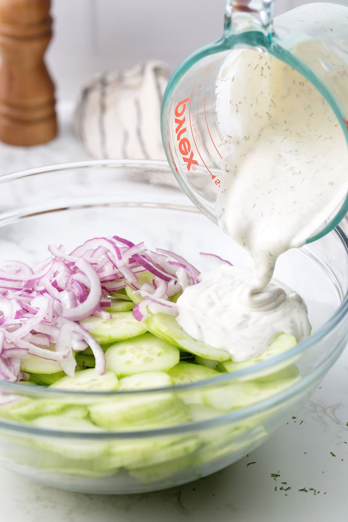 Creamy cucumber salad dressing poured into a mixing bowl with sliced cucumbers and red onions.