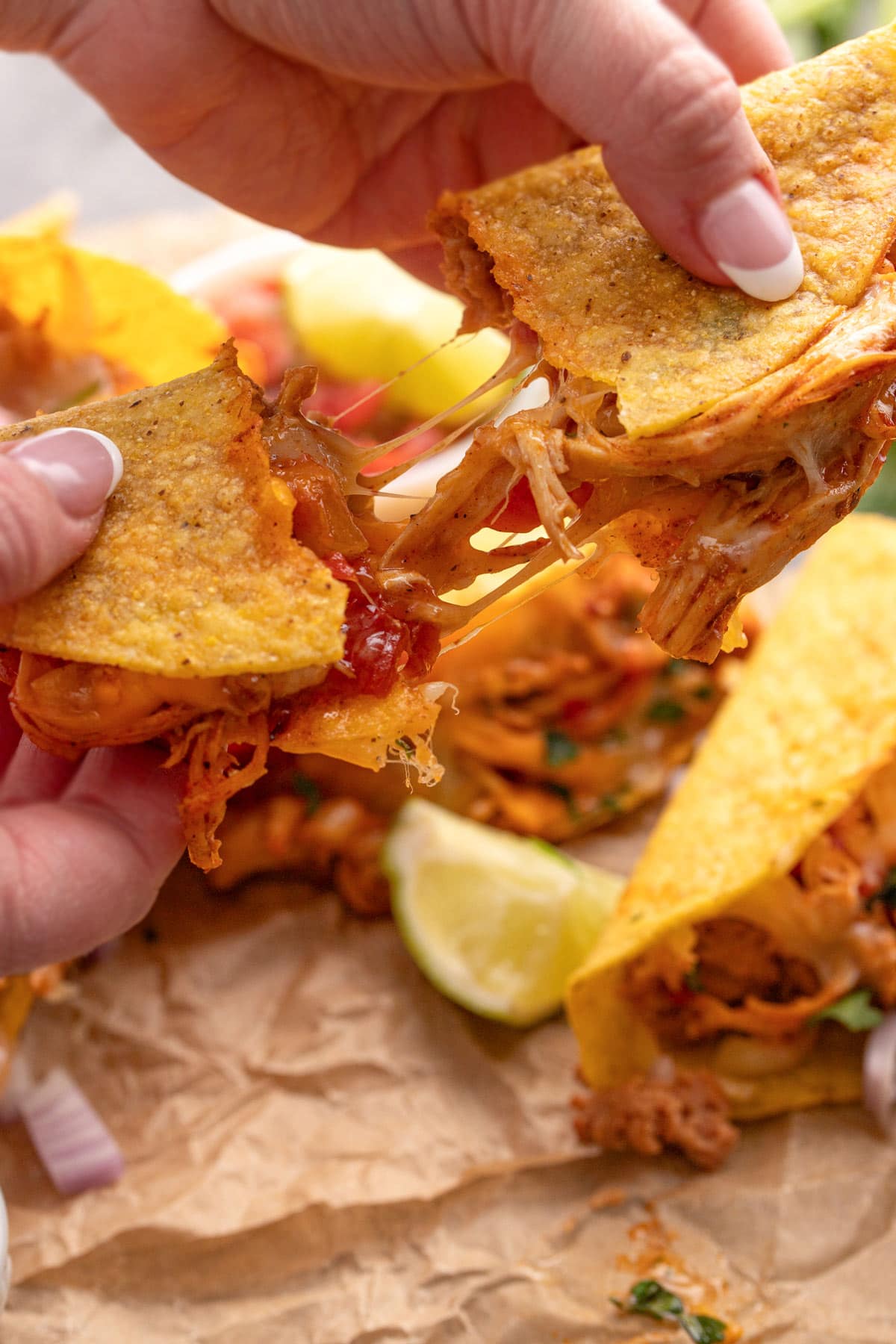 A baked chicken taco being pulled apart with cheese strings.