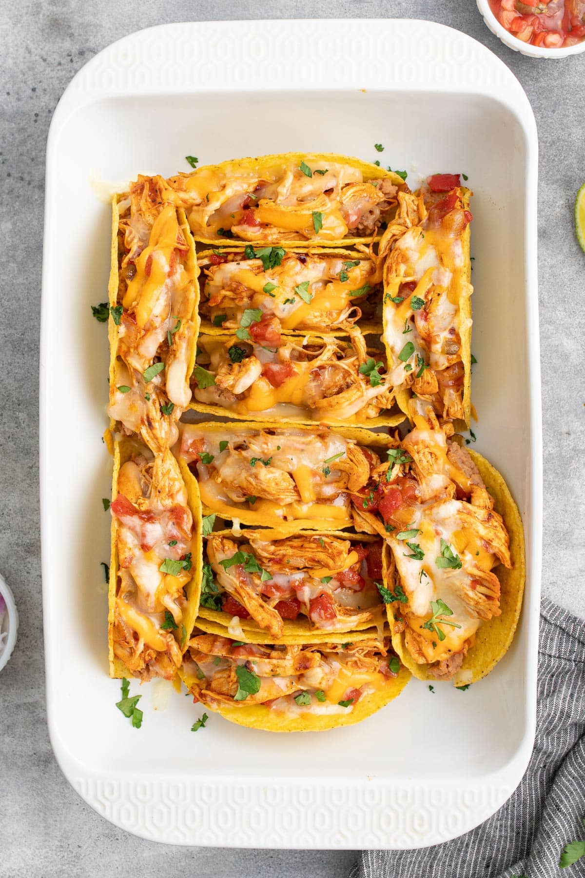Ten cheesy baked chicken tacos topped with chopped fresh cilantro in a white casserole dish.