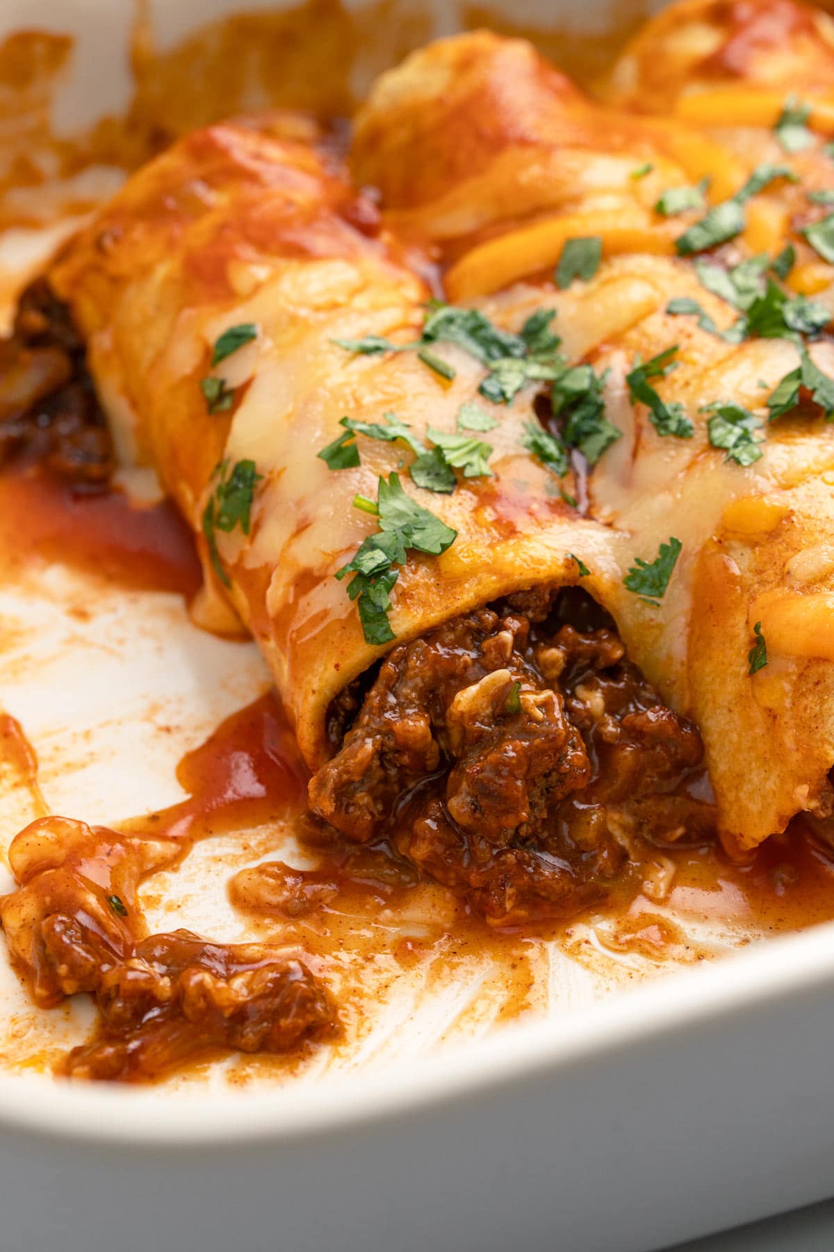 A close up shot of a beef enchilada with its filling spilling out.