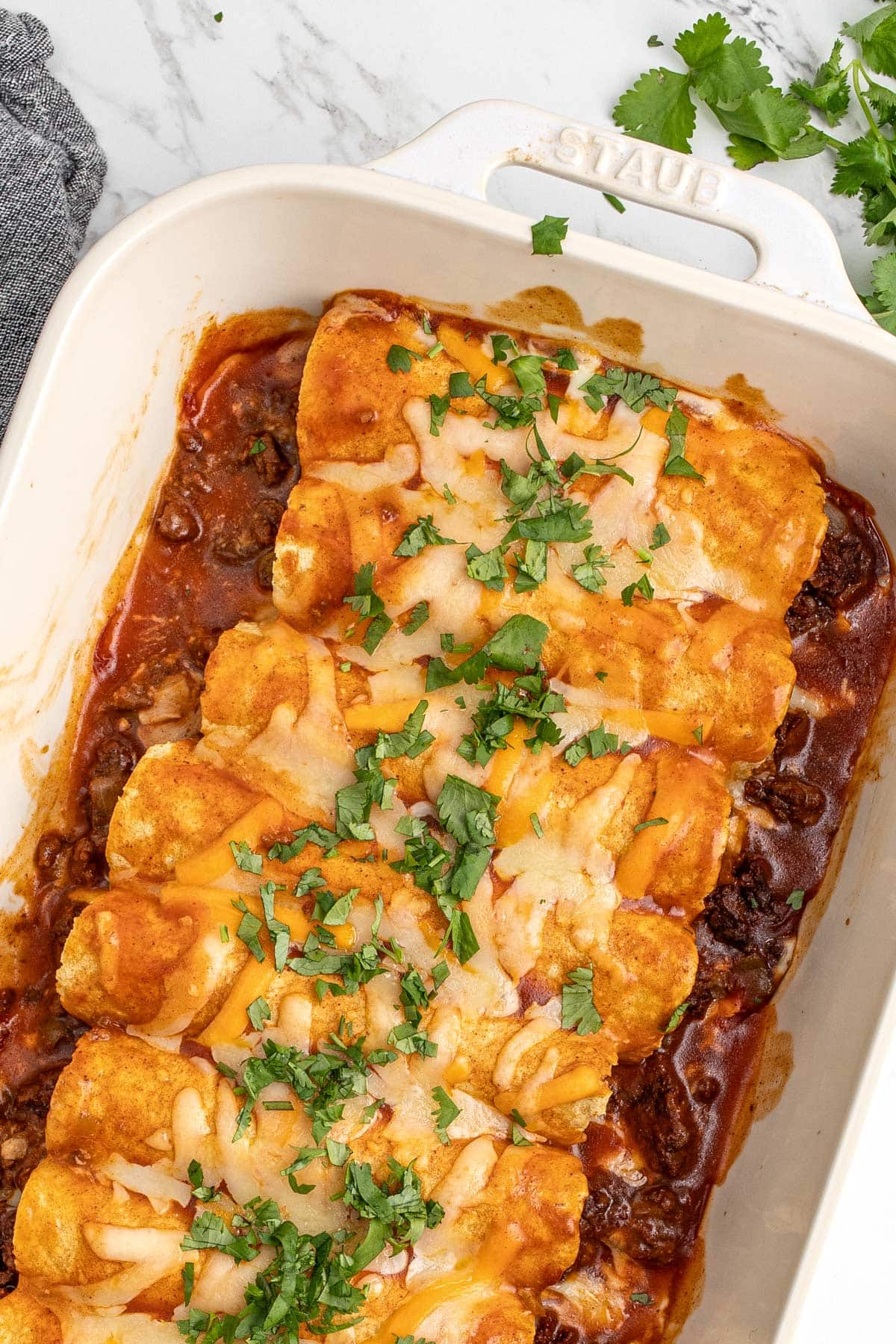 Several ground beef enchiladas lined in a single layer in a white casserole dish.