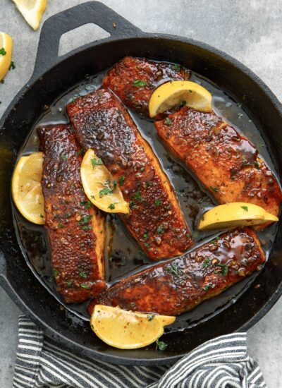 Honey glazed salmon fillets topped with lemon wedges and chopped parsley in a cast iron pan.
