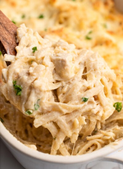 A generous serving of easy chicken tetrazzini lifted out of the casserole with a wooden spoon.