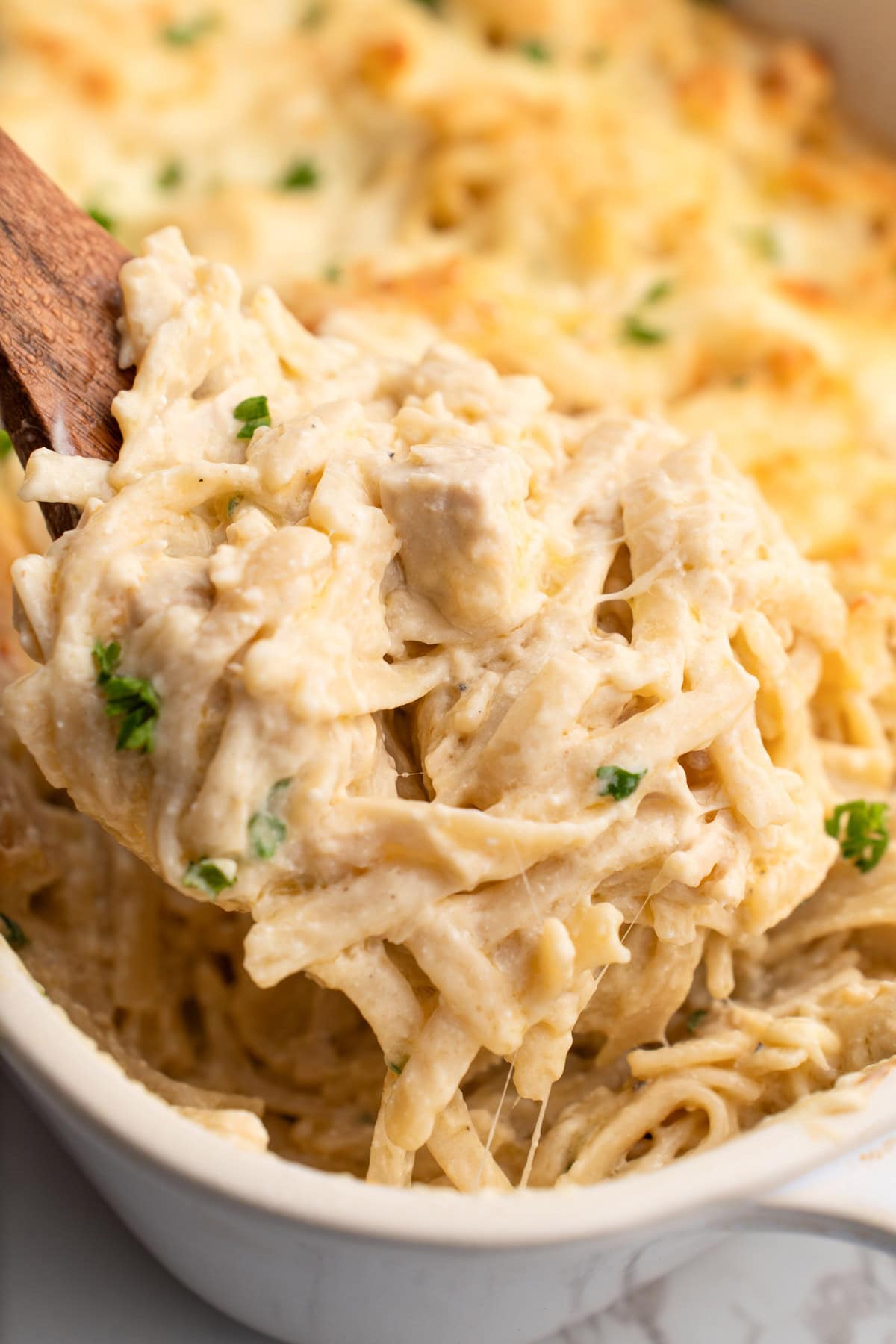 A generous serving of easy chicken tetrazzini lifted out of the casserole with a wooden spoon.