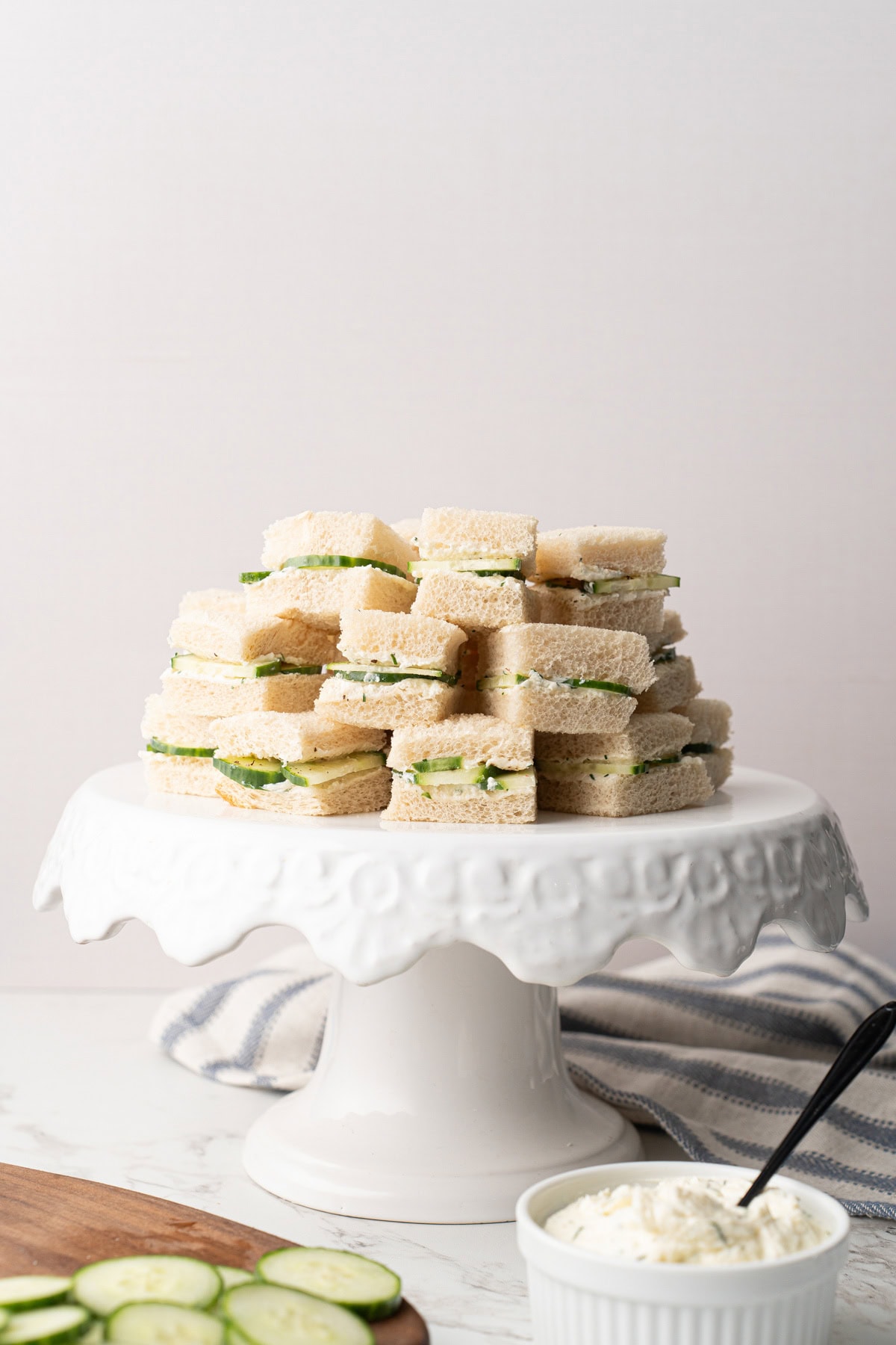 Several cucumber sandwiches stacked high on a white cake stand.