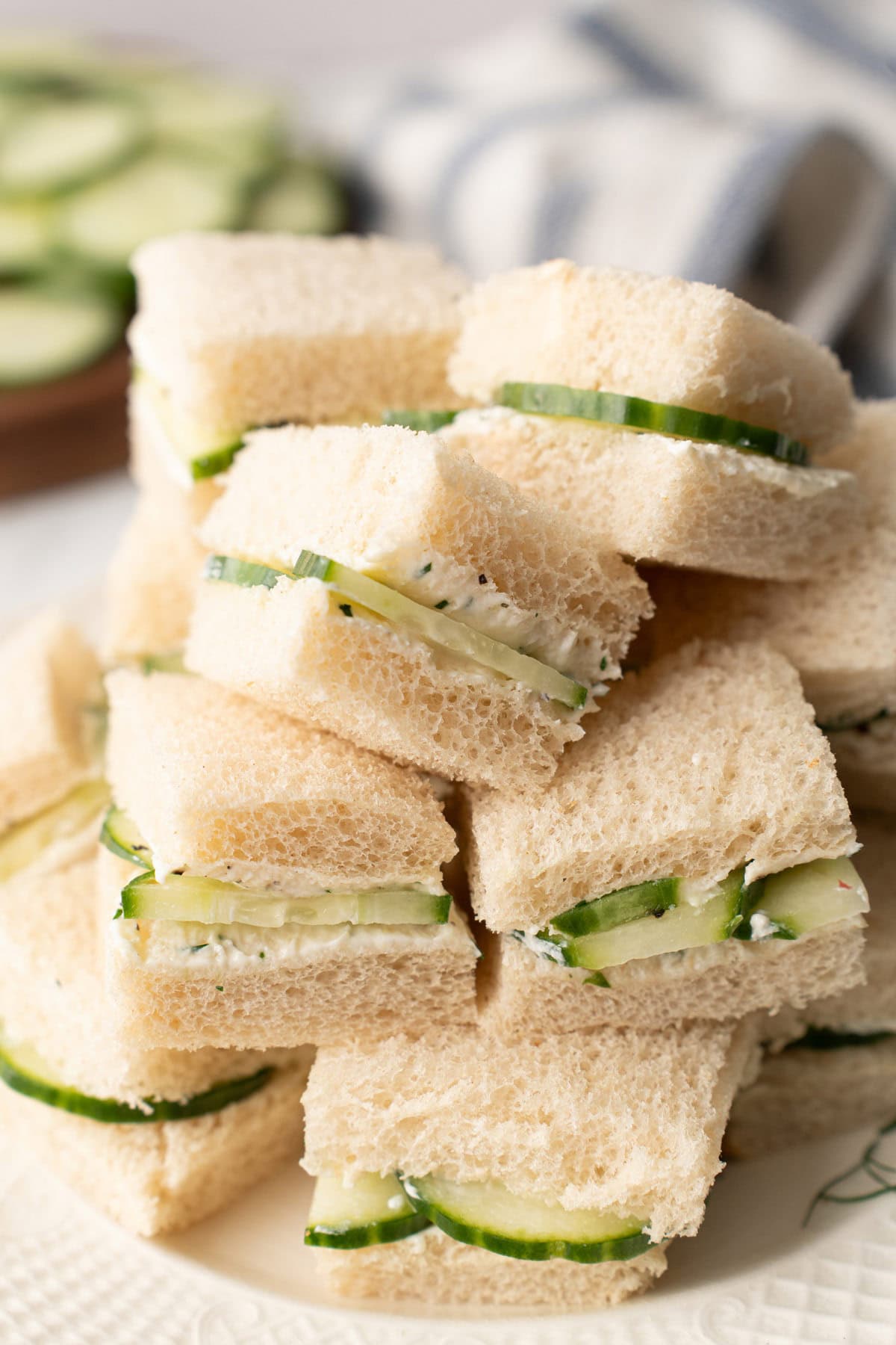 A close up of several cucumber sandwiches stacked high on a white plate.