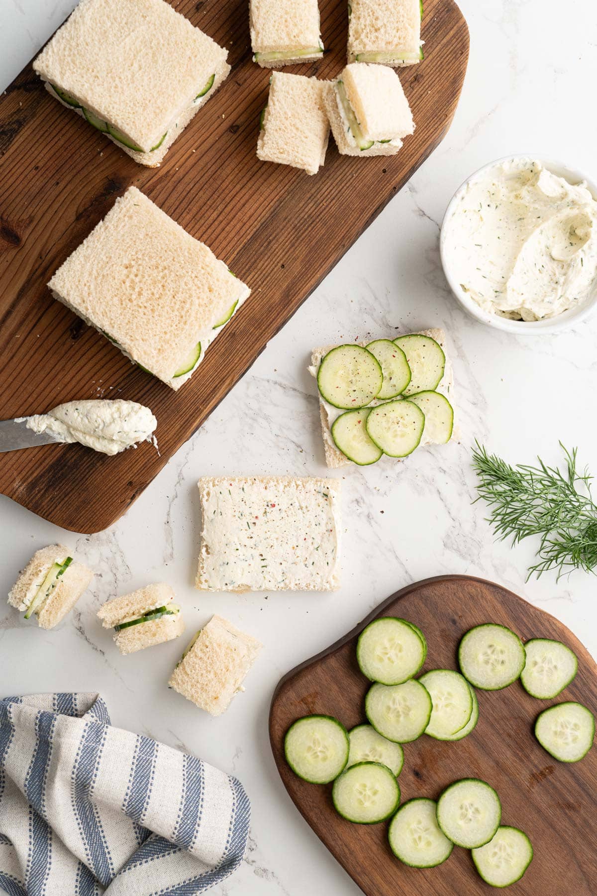 The process of making cucumber sandwiches with crustless bread slathered in cream cheese spread and thinly sliced cucumbers.